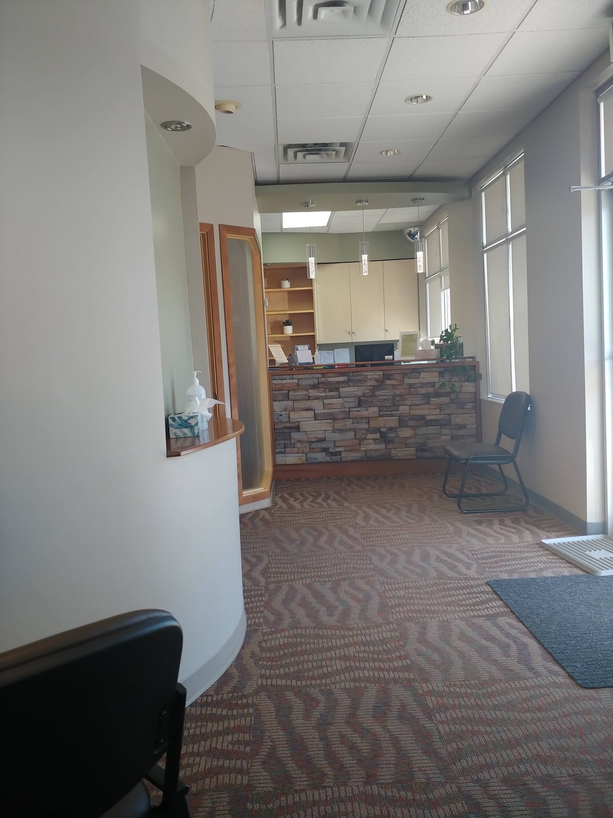 The reception at All West Dental, with a stone-clad front desk, daylit windows and a waiting chair
